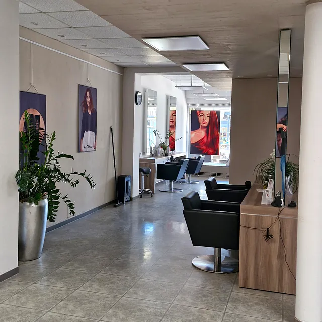 Ein Friseursalon mit mehreren Stühlen und einem großen Spiegel an der Wand. 
